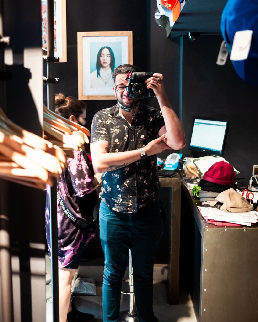 A man takes a photo inside a trendy clothing store featuring hanging garments.