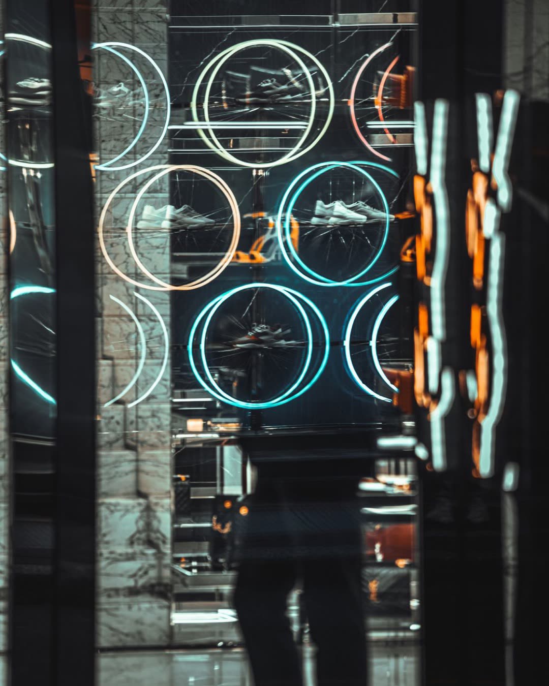 Urban store window with neon reflections and circular patterns creates a futuristic abstract vibe.