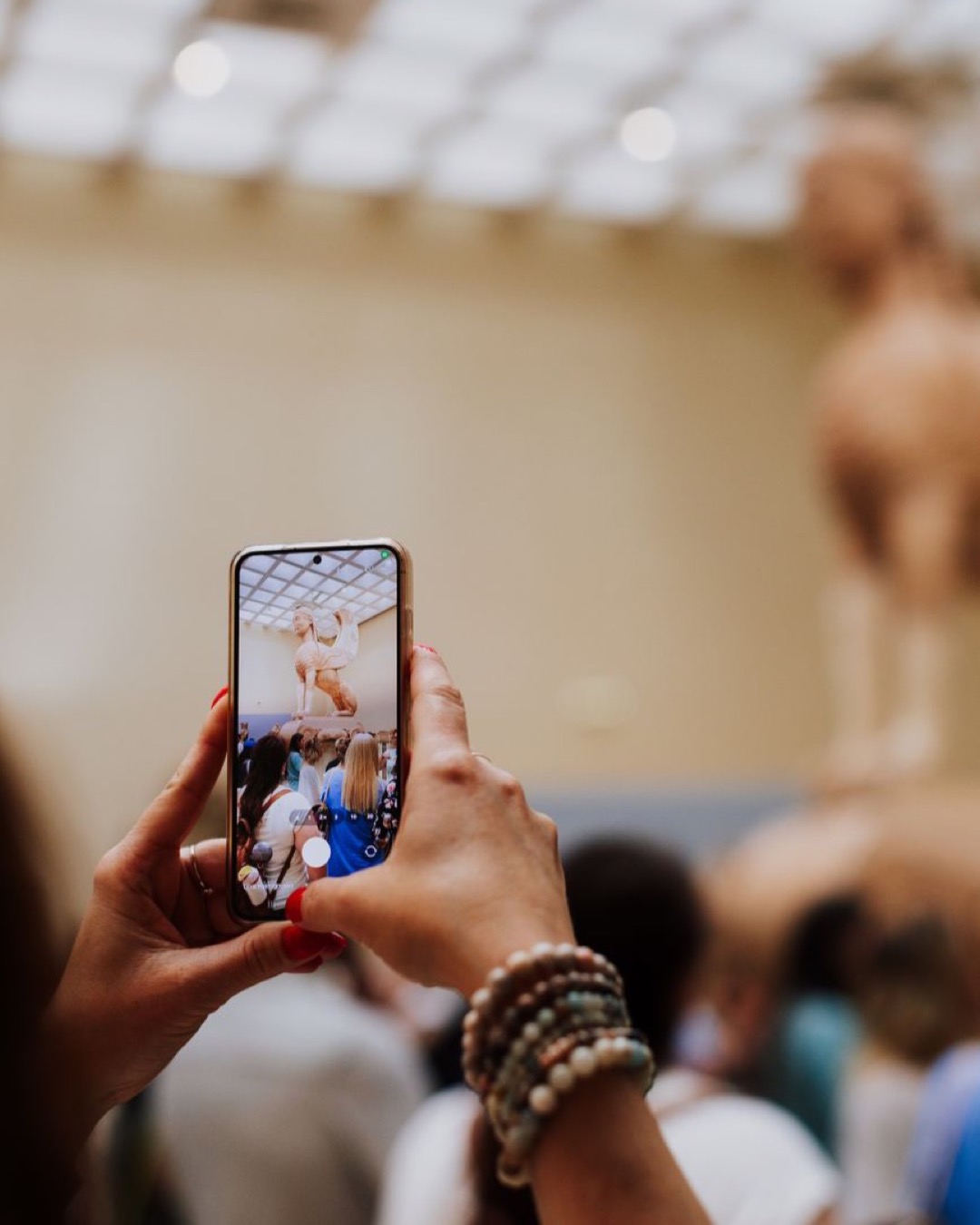 Visitor using smartphone to photograph a classical sculpture in a museum setting.