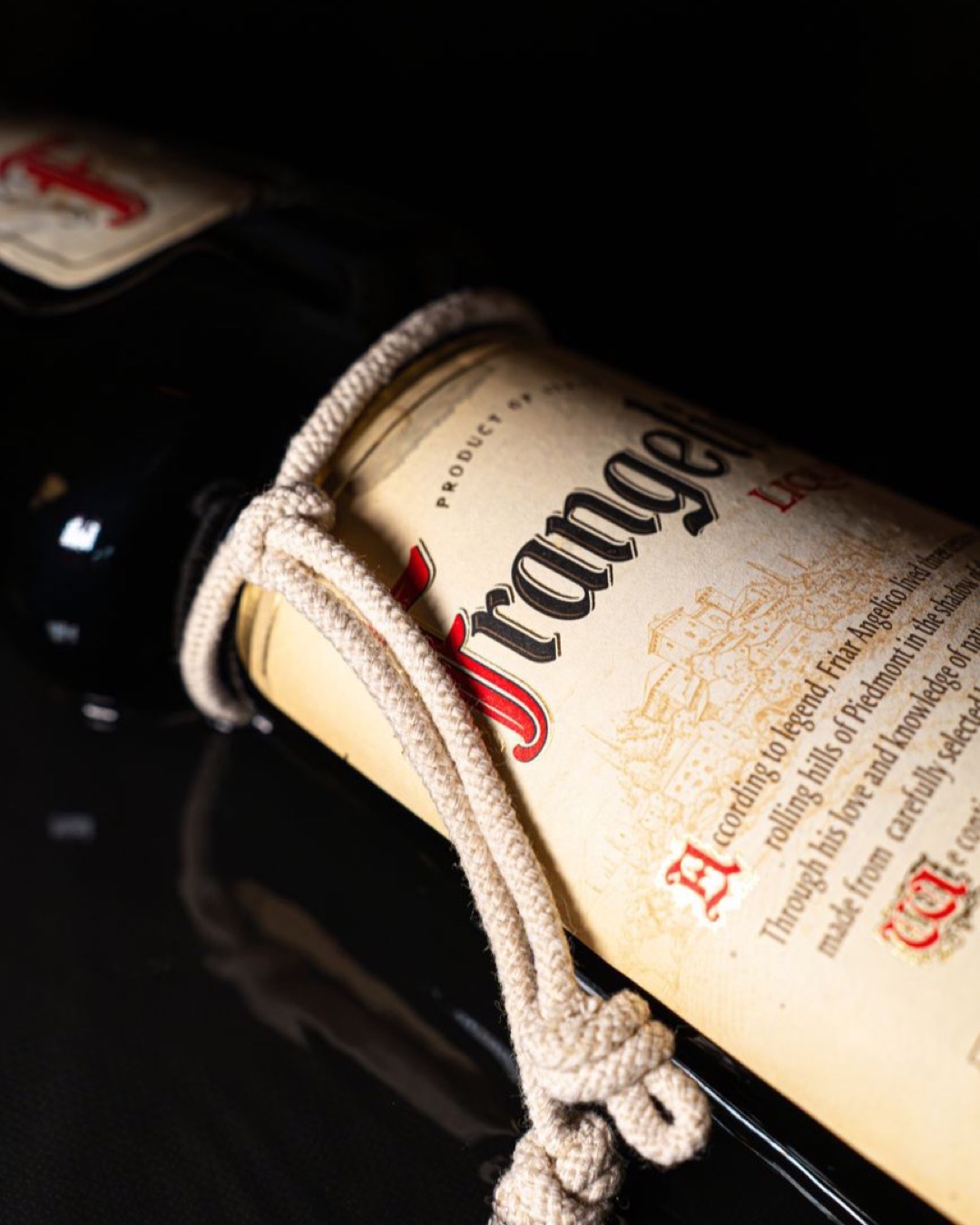Stylish liqueur bottle with label and rope detail photographed against a dark background.