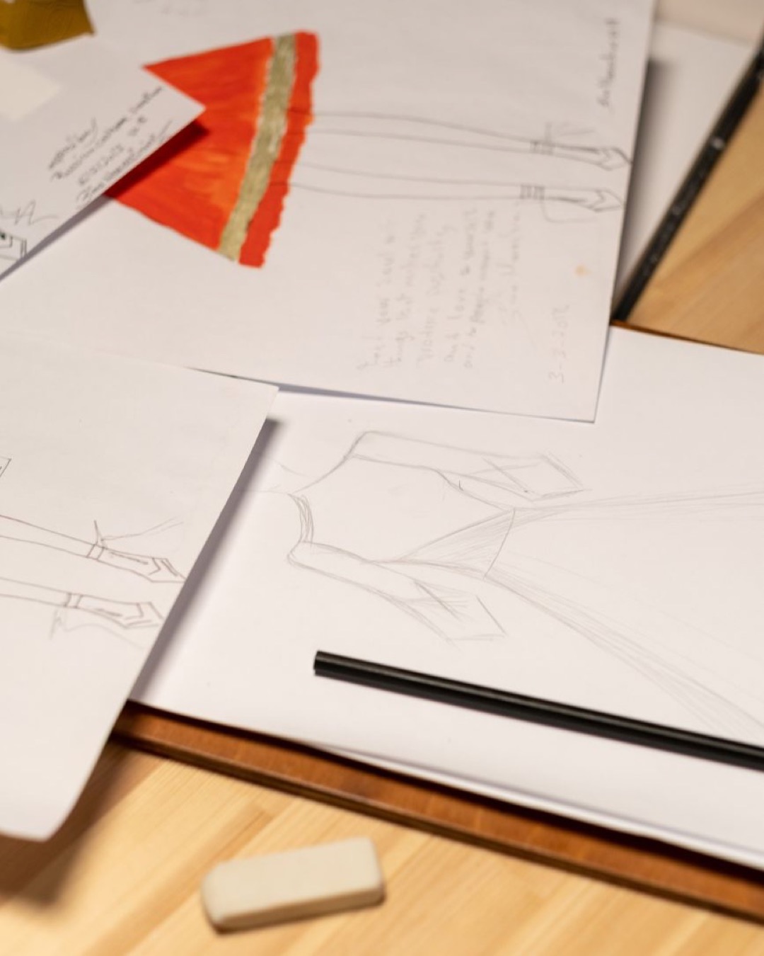 Close-up of fashion sketches on desk with pencil and eraser, highlighting the creative process.