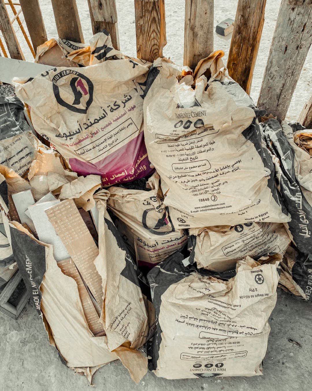 A pile of cement bags placed near a wooden fence, hinting at construction or renovation work.