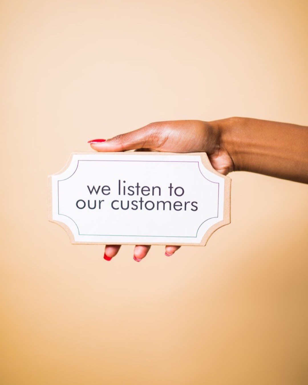 A hand holding a sign saying 'we listen to our customers' on a neutral background.