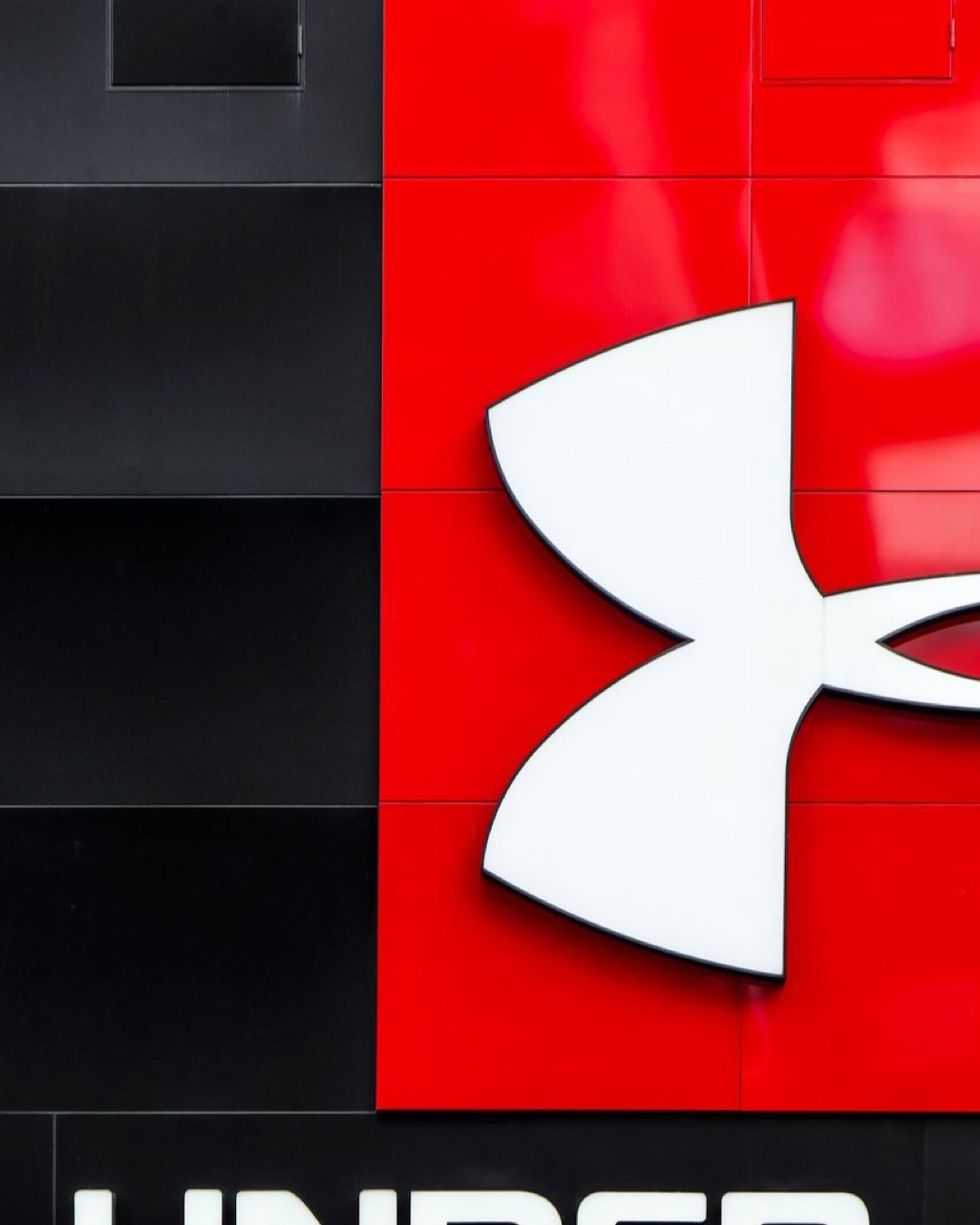 Close-up of Under Armour logo on a stylish red and black wall with modern graphic design elements.