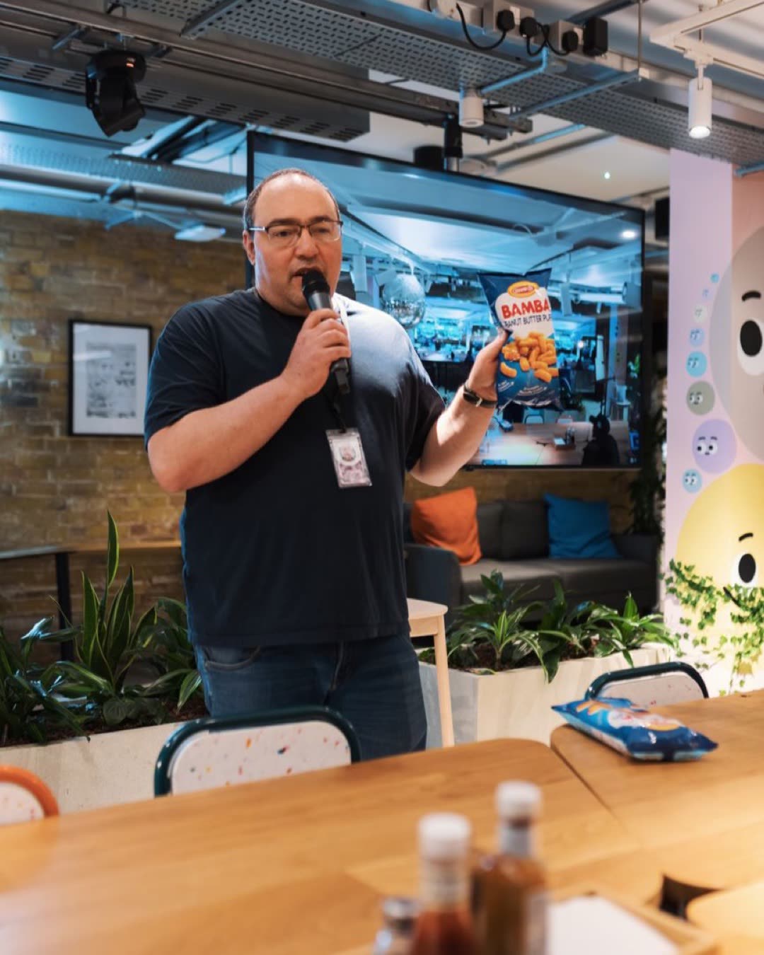 Man with microphone showcasing snack product in modern indoor space. Ideal for business or lifestyle themes.