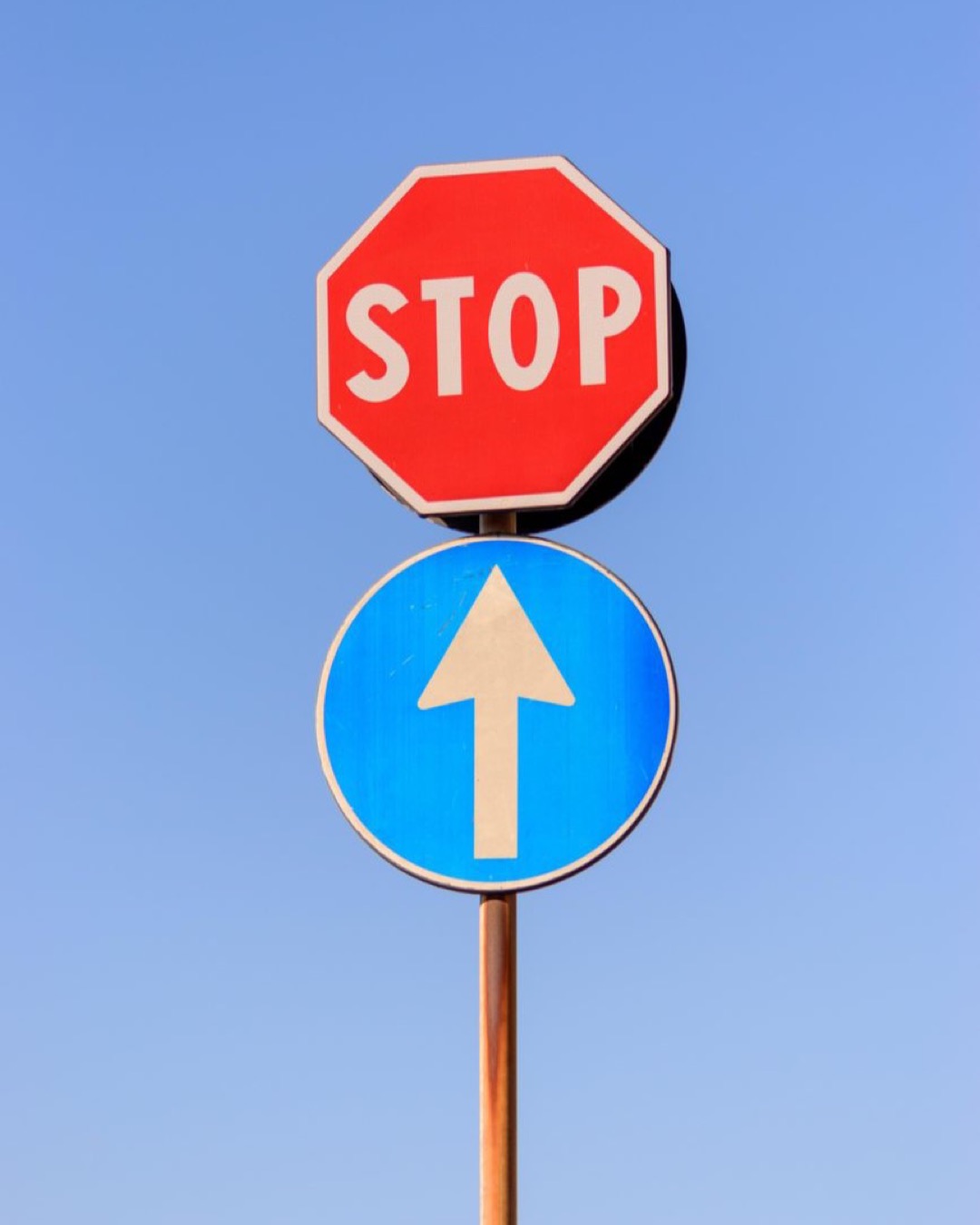 A red stop sign and blue forward arrow against a clear blue sky.