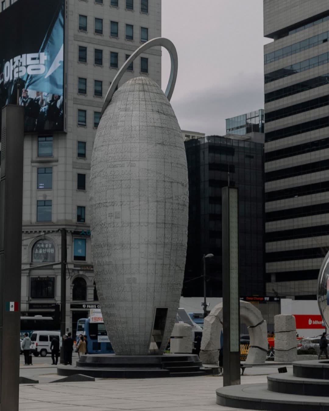 Modern sculpture in Seoul's bustling urban landscape with skyscrapers in view.