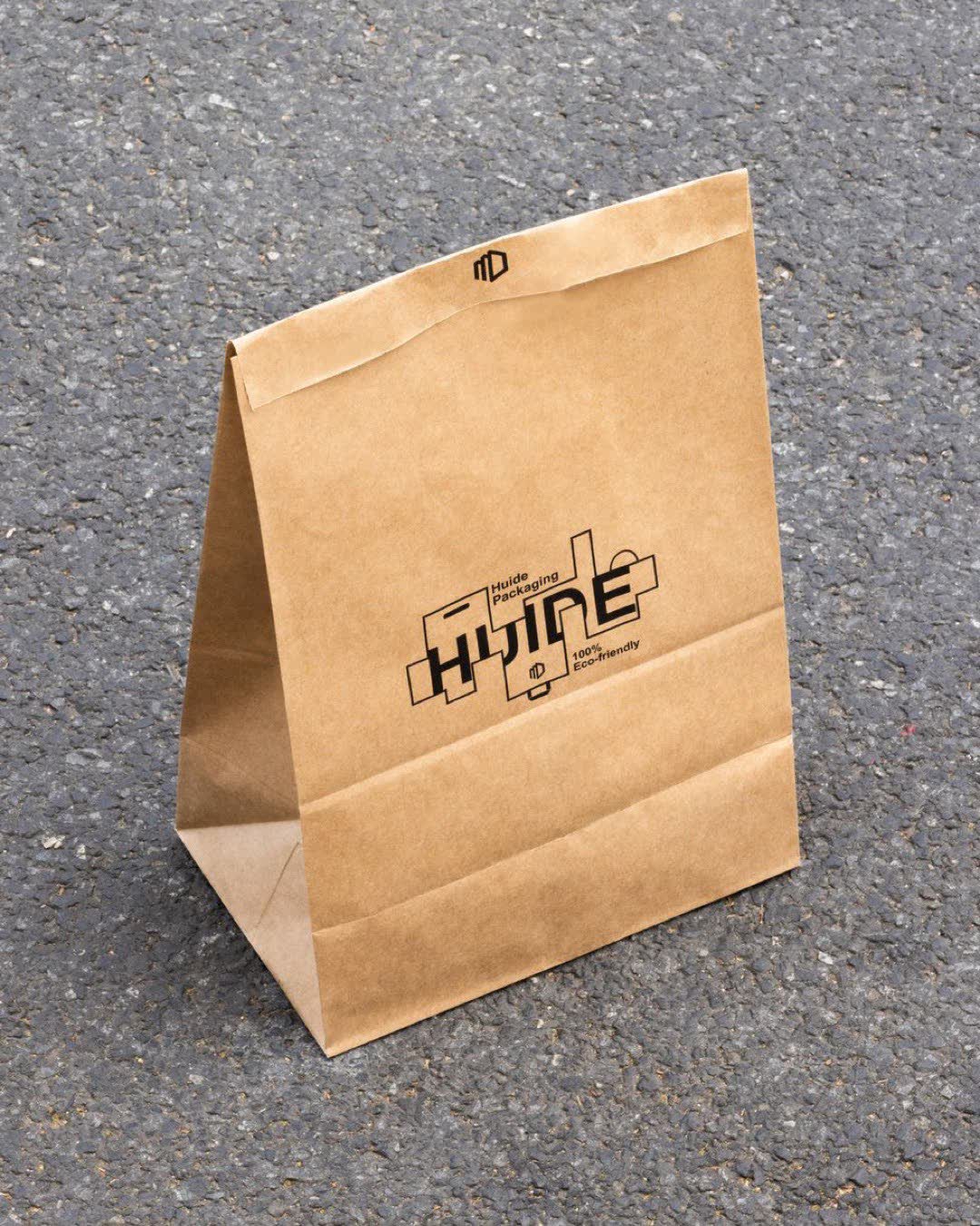 A standing kraft paper bag with custom print on a textured asphalt surface under sunlight.