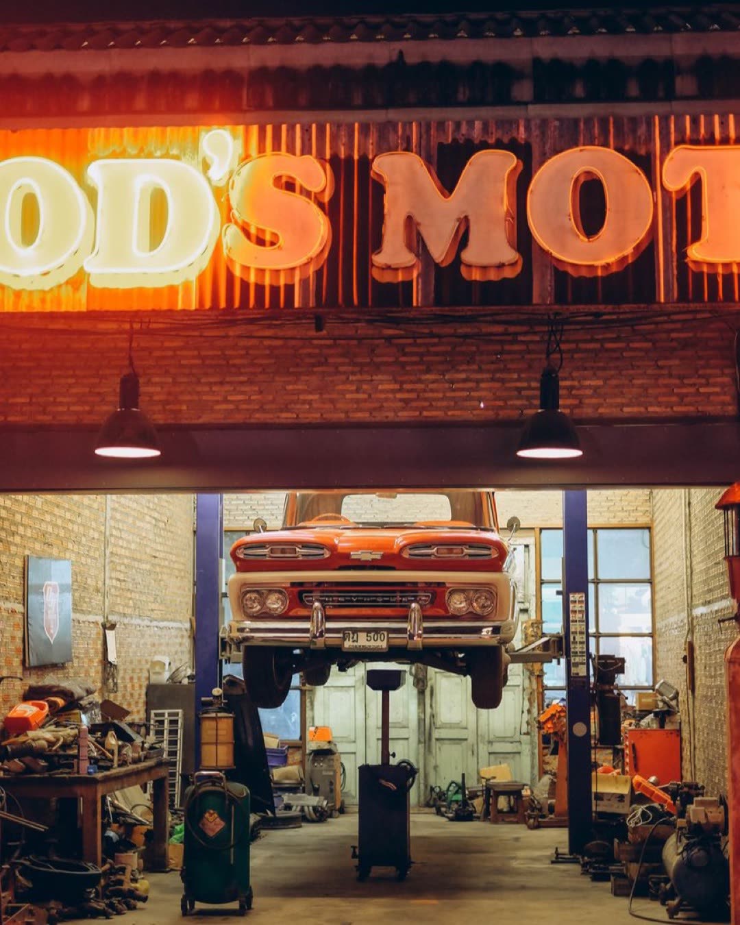 A classic car being repaired at a retro-style garage in Bangkok, Thailand at night.