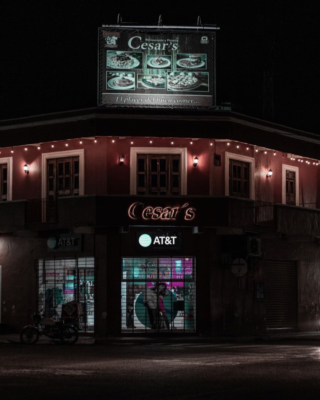 Urban nightscape featuring a restaurant's illuminated sign and street lights casting soft glow.