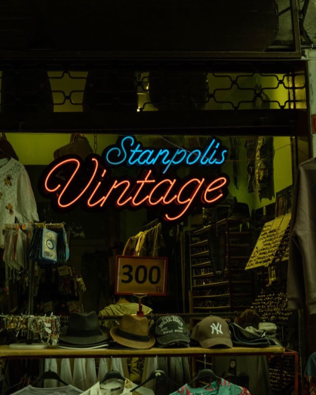 Vintage shop with neon sign and hats on display at night.