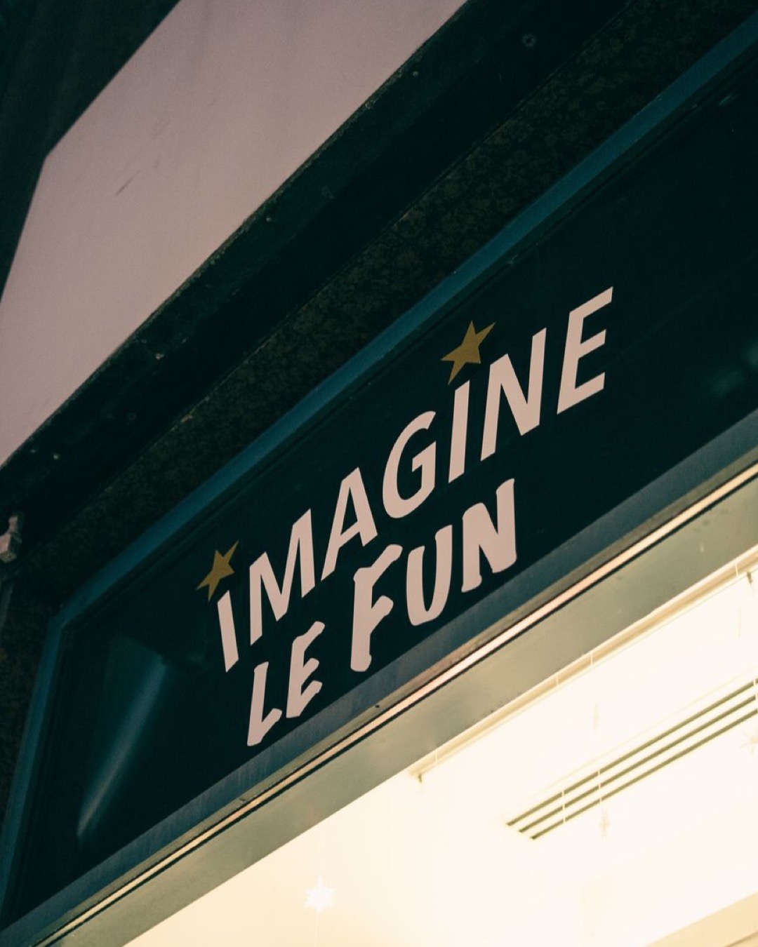 Close-up of 'Imagine Le Fun' shop sign illuminated at night, showcasing urban nightlife charm.