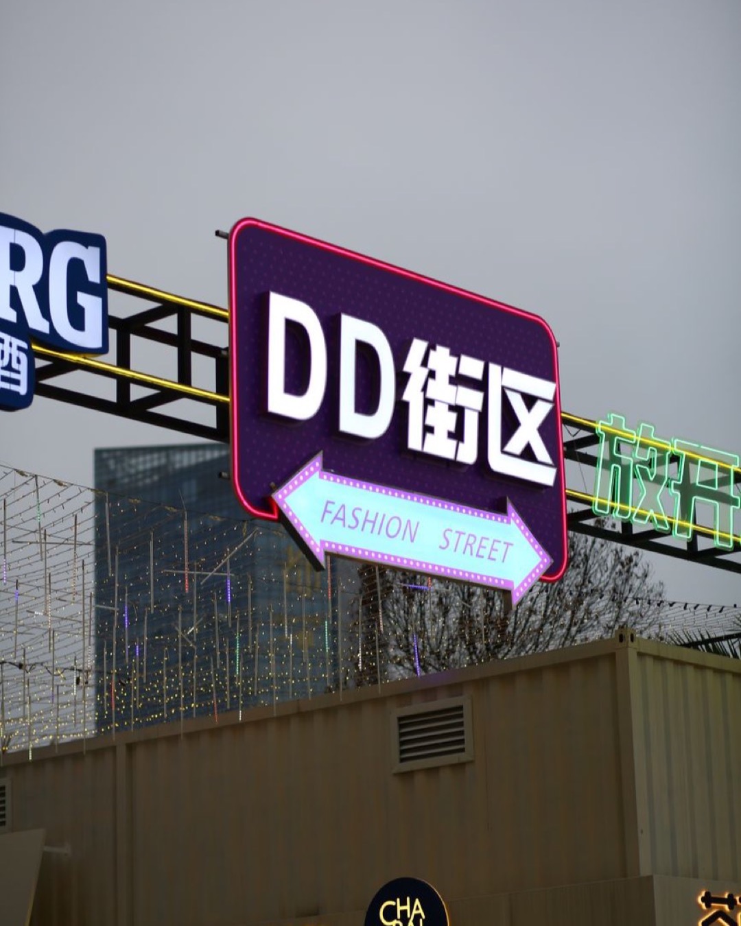 Vertical shot of a brightly lit Fashion Street sign against an urban backdrop.