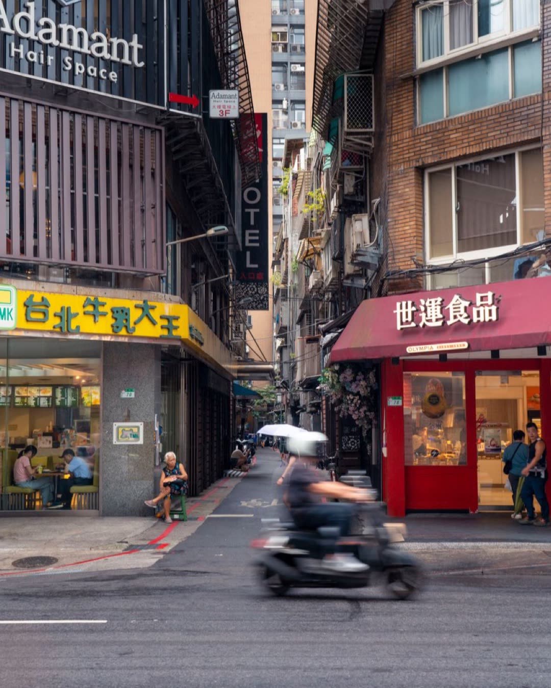 Dynamic street view in Taipei, featuring local shops and a scooter speeding by in a busy urban setting.