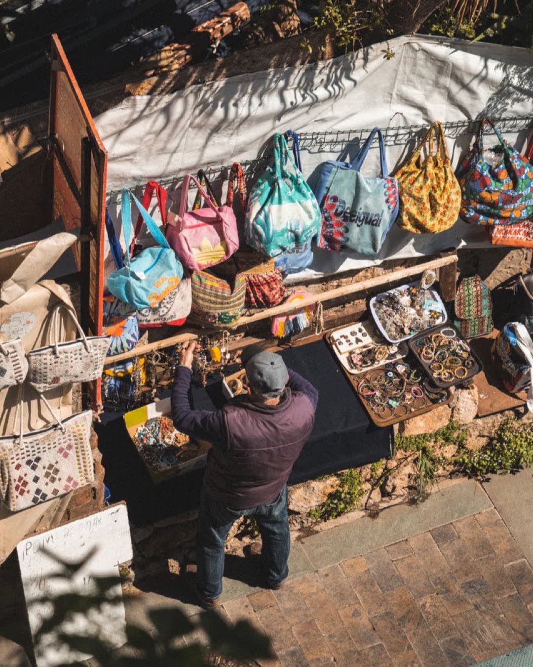 Overhead view of a vibrant market stall displaying handmade bags and crafts on a sunny day.