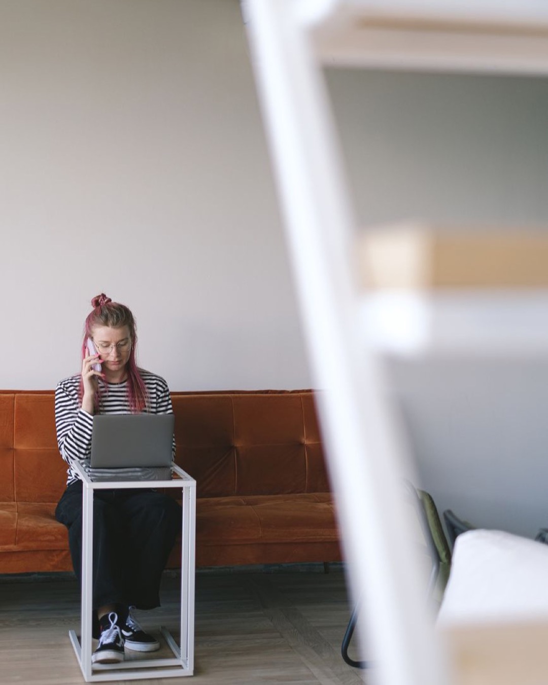 Young woman with pink hair working on laptop in stylish hotel room, embodying the freelance lifestyle.