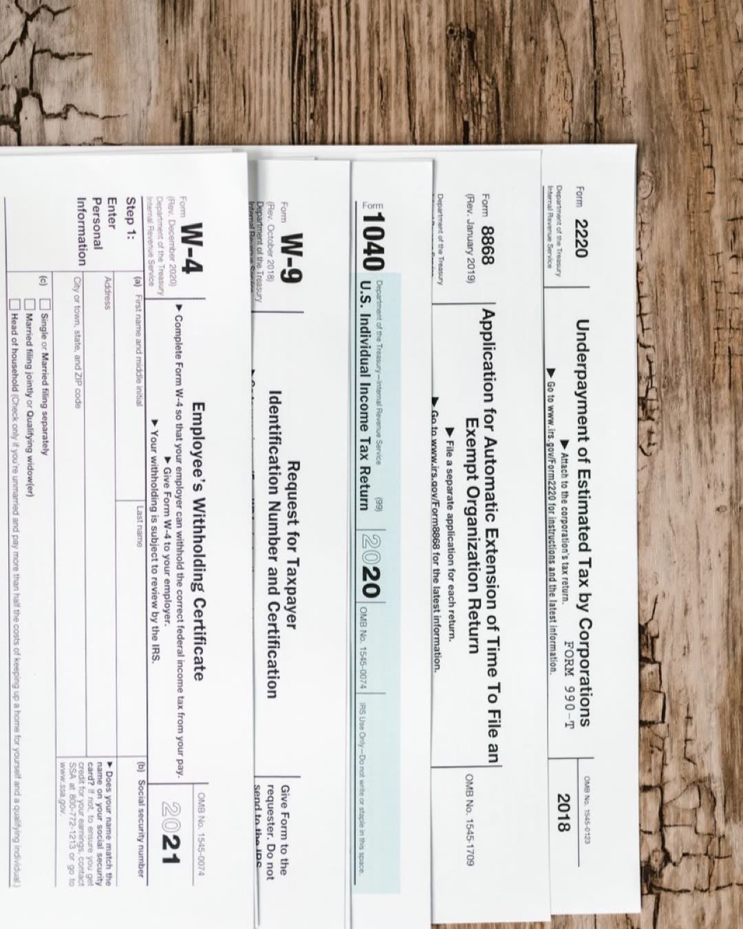 Close-up of various U.S. tax forms including W-4, W-9, and 1040 on a rustic wooden surface.