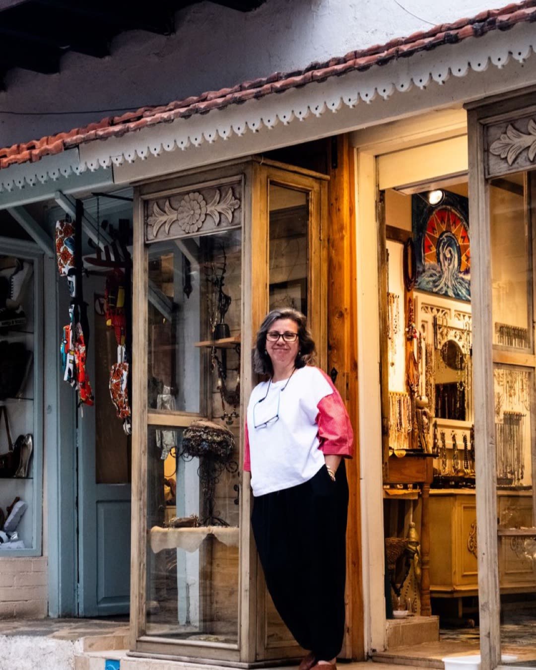 A friendly shop owner stands outside a rustic artisan store, showcasing crafts and souvenirs.